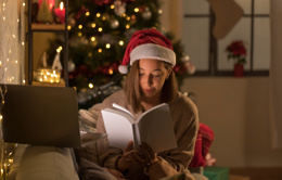 woman with santa hat reading book front laptop